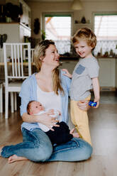 A beautiful young mother with a newborn baby and his toddler brother at home. - HPIF24332