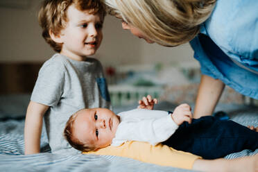 Eine schöne junge Mutter mit einem neugeborenen Baby und seinem kleinen Bruder, die sich zu Hause unterhalten. - HPIF24334