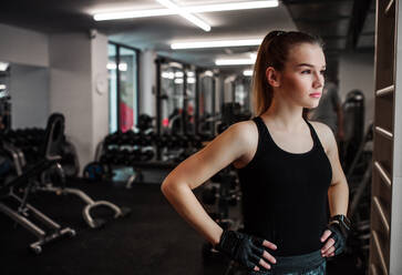 A portrait of a beautiful young girl or woman standing in a gym, hands on hips. - HPIF24341