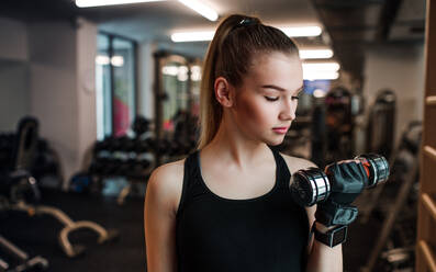 Ein junges Mädchen oder eine junge Frau mit Hanteln, die in einem Fitnessstudio trainieren. - HPIF24343