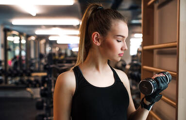 Ein junges Mädchen oder eine junge Frau mit Hanteln, die in einem Fitnessstudio trainieren. - HPIF24344