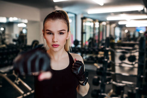 Vorderansicht eines jungen Mädchens oder einer Frau mit Handschuhen, die in einem Fitnessstudio trainieren. - HPIF24347