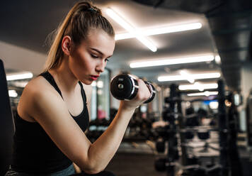 Ein junges Mädchen oder eine junge Frau mit Hanteln, die in einem Fitnessstudio trainieren. - HPIF24352