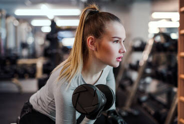 Ein junges Mädchen oder eine junge Frau mit Hanteln, die in einem Fitnessstudio trainieren. - HPIF24359