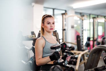 Ein junges Mädchen oder eine junge Frau mit Hanteln, die in einem Fitnessstudio trainieren. - HPIF24364
