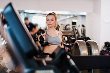 Ein junges Mädchen oder eine junge Frau mit Hanteln, die in einem Fitnessstudio trainieren. - HPIF24365