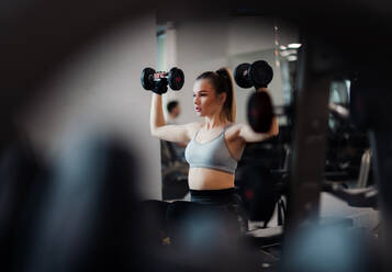 A young girl or woman with dumbbells, doing workout in a gym. - HPIF24369