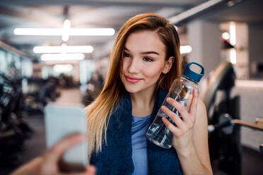 Eine junge Frau in einem Fitnessstudio macht ein Selfie mit ihrer Wasserflasche und ihrem Smartphone - HPIF24387