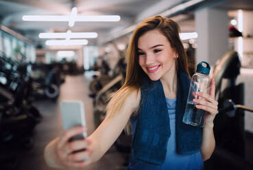 A young woman in a gym takes a selfie with her water bottle and smartphone - HPIF24389