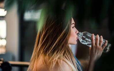 Seitenansicht eines jungen Mädchens oder einer Frau, die in einer Turnhalle steht und Wasser aus einer Flasche trinkt. - HPIF24393