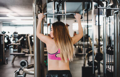 A rear view of a beautiful young girl or woman doing strength workout in a gym. - HPIF24397