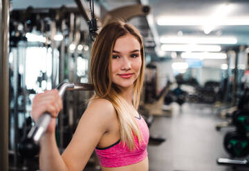 Eine Seitenansicht eines schönen jungen Mädchens oder einer Frau beim Krafttraining in einem Fitnessstudio. - HPIF24401