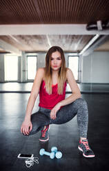 A portrait of a beautiful young girl or woman with dumbbells and smartphone in a gym. - HPIF24427