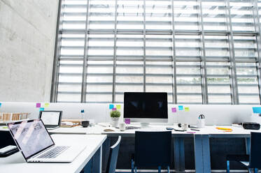 Ein Interieur von Schreibtischen mit Computer und Modell eines Hauses in einem modernen geräumigen Büro. - HPIF24459