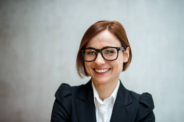 Ein Porträt einer jungen, fröhlichen Geschäftsfrau, die in einem Büro steht und in die Kamera schaut. - HPIF24500