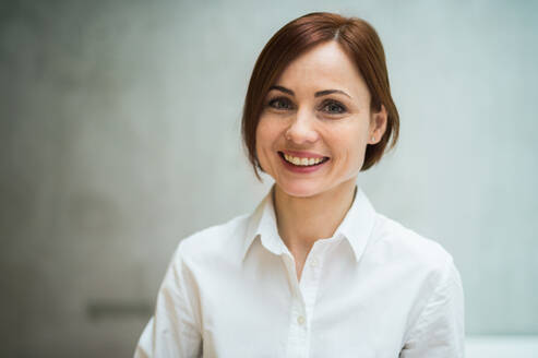 Ein Porträt einer jungen, fröhlichen Geschäftsfrau, die in einem Büro steht und in die Kamera schaut. - HPIF24503