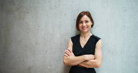 A portrait of young cheerful businesswoman standing in office, arms crossed. Copy space. - HPIF24509