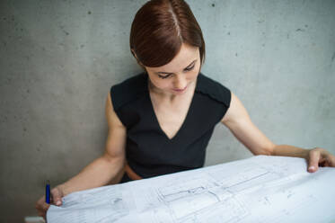 Eine junge Geschäftsfrau oder Architektin, die in einem Büro steht und sich Baupläne ansieht. - HPIF24527