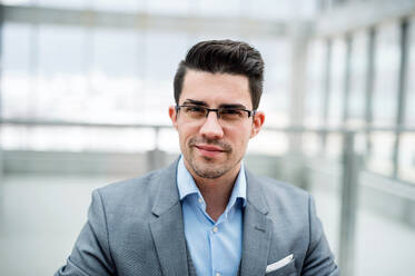 A front vire of portrait of young businessman indoors in an office. A close-up. - HPIF24535