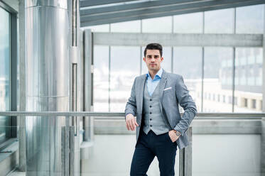 A handsome hipster young man with formal suit standing by a window