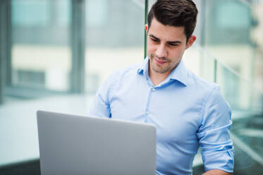 A portrait of young handsome businessman with laptop sitting in office. - HPIF24547