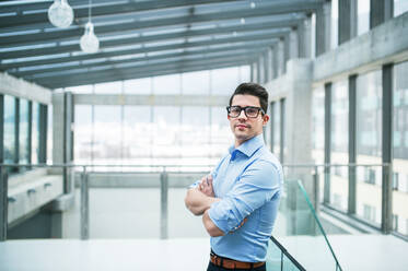 A portrait of young businessman standing indoors in an office, arms crossed. Copy space. - HPIF24551