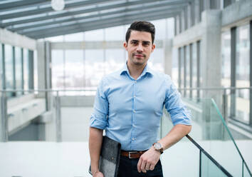 A young businessman standing in corridor outside office, looking at camera. - HPIF24552