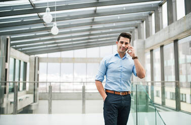 A side view of young businessman with smartphone in an office, making a phone call. Copy space. - HPIF24555