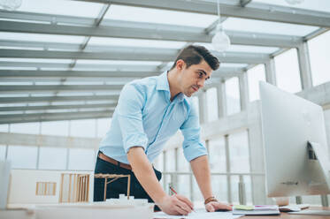 Young businessman or architect with model of a house standing at the desk in office, working. - HPIF24558