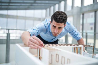 Young businessman or architect with model of a house standing at the desk in office, working. - HPIF24561