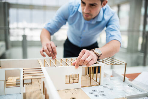 Junger Geschäftsmann oder Architekt mit Modell eines Hauses, der am Schreibtisch im Büro steht und arbeitet. - HPIF24562