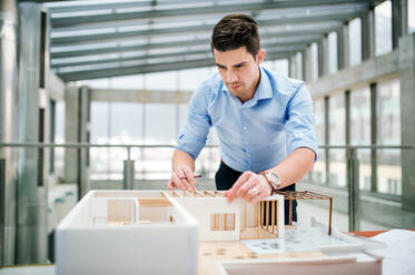 Young businessman or architect with model of a house standing at the desk in office, working. - HPIF24563