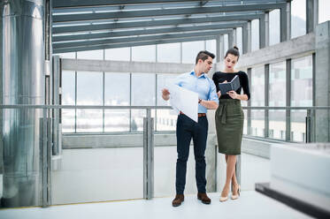 Two young male and female architects with blueprints standing in office, talking. - HPIF24569