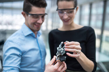 Two young businesspeople or scientists with protective glasses and robotic hand standing in office, talking. - HPIF24577