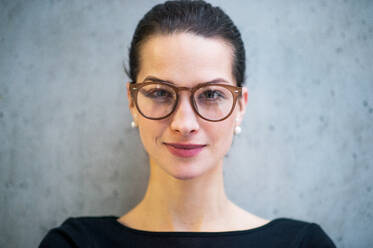 Ein Porträt einer jungen Geschäftsfrau mit Brille, die in einem Büro steht und in die Kamera schaut. - HPIF24587