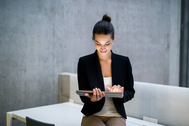 A portrait of a young student or businesswoman sitting on desk in room in a library or office, using tablet. - HPIF24594