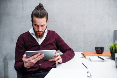 Ein junger Geschäftsmann mit Tablet sitzt am Schreibtisch im Büro und arbeitet. - HPIF24623