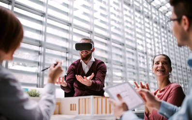 A group of young architects with model of a house and VR goggles working in office, talking. - HPIF24648