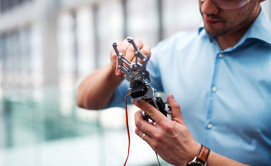 Ein Mittelteil eines jungen Geschäftsmannes oder Wissenschaftlers mit Roboterhand und Schutzbrille, der in einem Büro steht und arbeitet. - HPIF24670