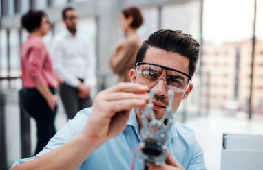 A young businessman or scientist with robotic hand and safety glasses standing in office, working. - HPIF24679