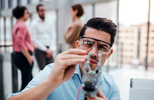 Ein junger Geschäftsmann oder Wissenschaftler mit Roboterhand und Schutzbrille steht im Büro und arbeitet. - HPIF24679