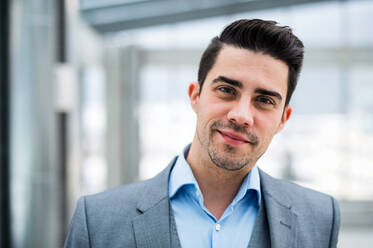 A portrait of young businessman standing indoors in an office. Copy space. - HPIF24701