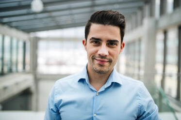 A portrait of young businessman standing indoors in an office. Copy space. - HPIF24702