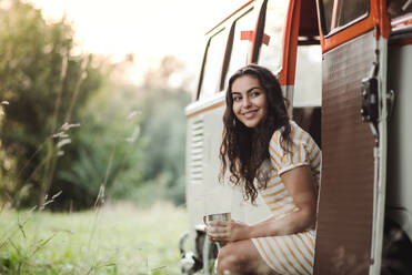 Ein fröhliches junges Mädchen mit Kaffee, das auf einem Roadtrip durch die Landschaft an einem Auto steht. copy space. - HPIF24715