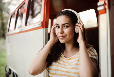Ein junges Mädchen mit Kopfhörern an einem Auto auf einem Roadtrip durch die Landschaft, das Musik hört. - HPIF24720