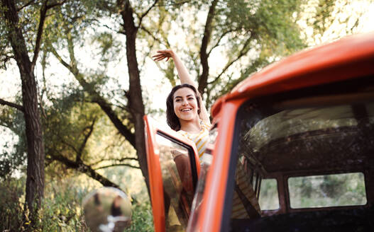 Ein fröhliches junges Mädchen auf einem Roadtrip durch die Landschaft, das jemandem aus einem Auto zuwinkt. - HPIF24726