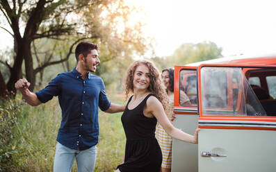 Eine Gruppe junger Freunde steht neben einem Retro-Minivan auf einem Roadtrip durch die Landschaft. - HPIF24736