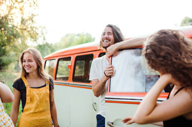 Eine Gruppe junger Freunde steht neben einem Retro-Minivan auf einem Roadtrip durch die Landschaft. - HPIF24738