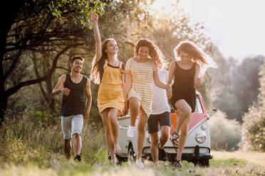 Eine Gruppe junger Freunde geht vor einem Retro-Minivan auf einem Roadtrip durch die Landschaft spazieren. - HPIF24746