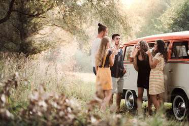 Eine Gruppe junger Freunde steht mit Getränken im Freien auf einem Roadtrip durch die Landschaft und trinkt aus Flaschen. - HPIF24749